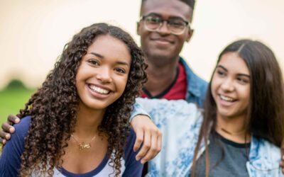 Three teenagers stand out in the open with smiles on their faces.
